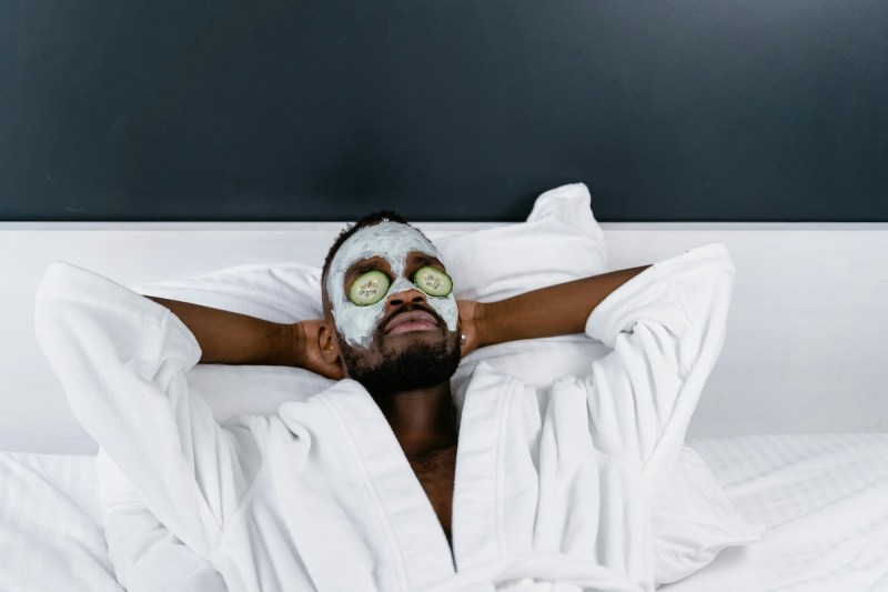 Man with white plush robe and cucumbers on his eyes