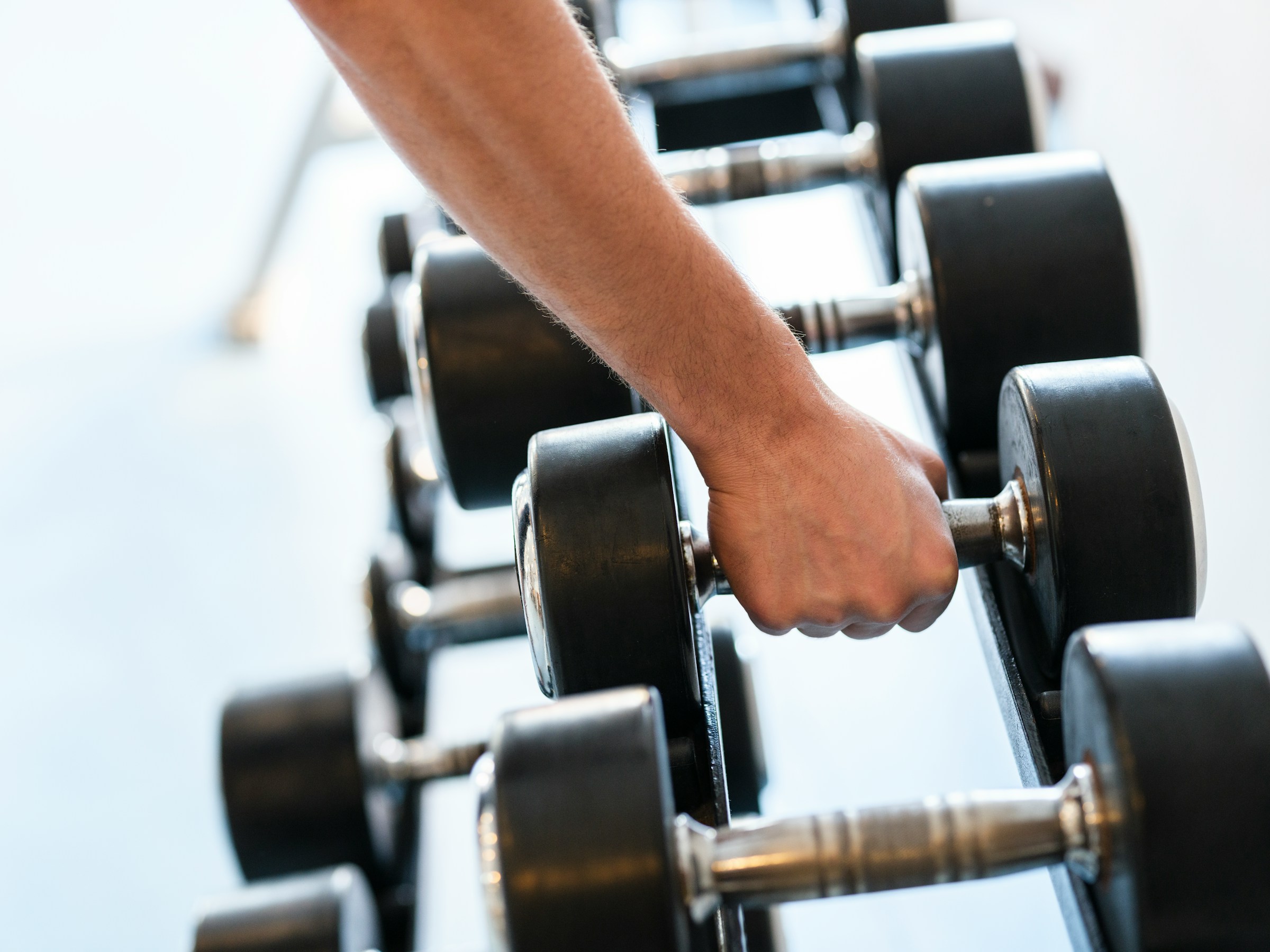 close up man hand grabbing dumbbell from rack weight rack in gym